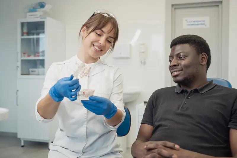 A smiling dentist shows a patient a tooth model during a relaxed checkup