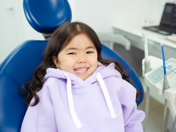 A cheerful young girl sitting in a blue dental chair before her checkup