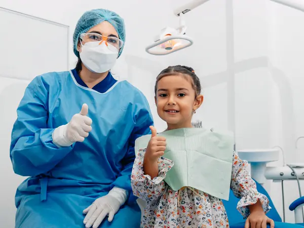A young girl and her dentist give a thumbs up after a checkup