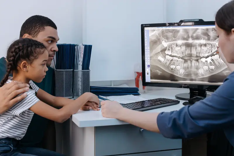 A dad and his daughter look at dental X-rays on a screen while the dentist explains them