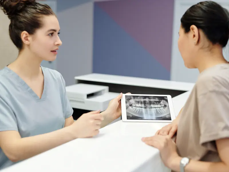 A dentist shows a patient her X-ray on a tablet at the front desk