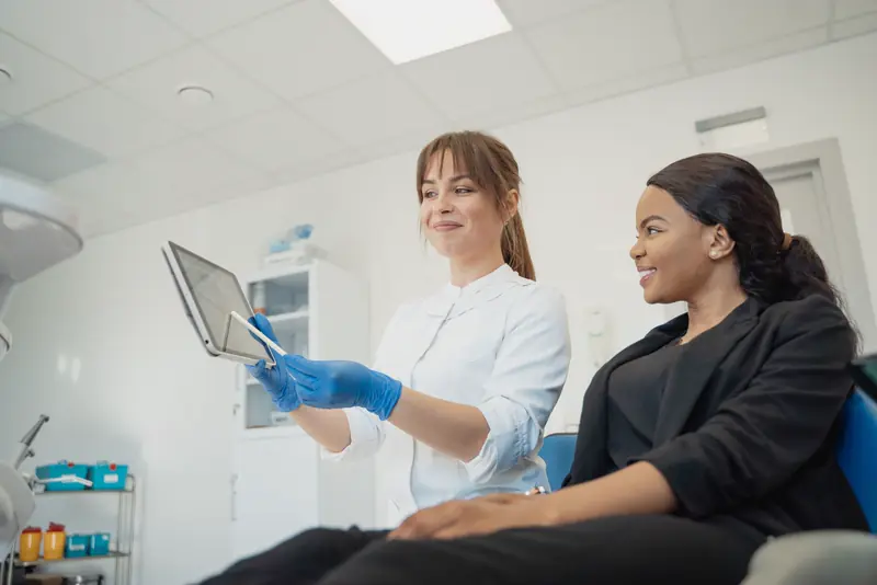 A dentist reviews a treatment plan on a tablet with a smiling patient