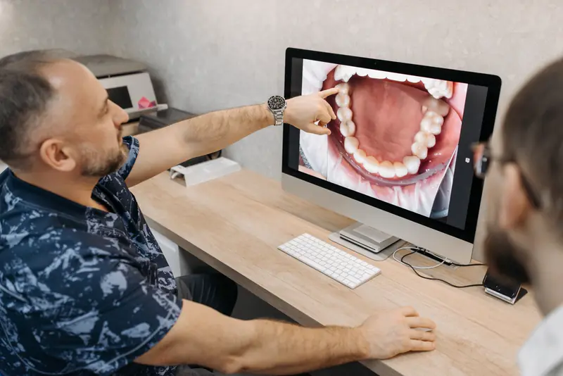 A dentist points to a close-up photo of teeth on a large monitor
