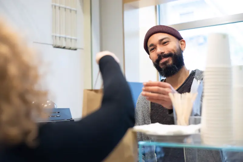 A smiling barista hands a paper bag of coffee across the café counter