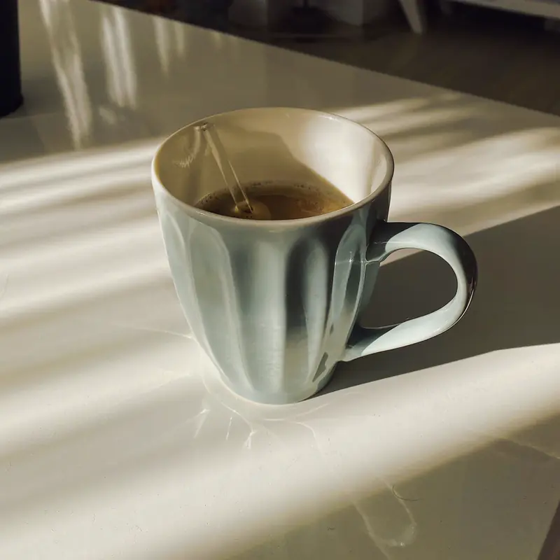 A ribbed ceramic cup of coffee on a sunny table, casting a soft shadow