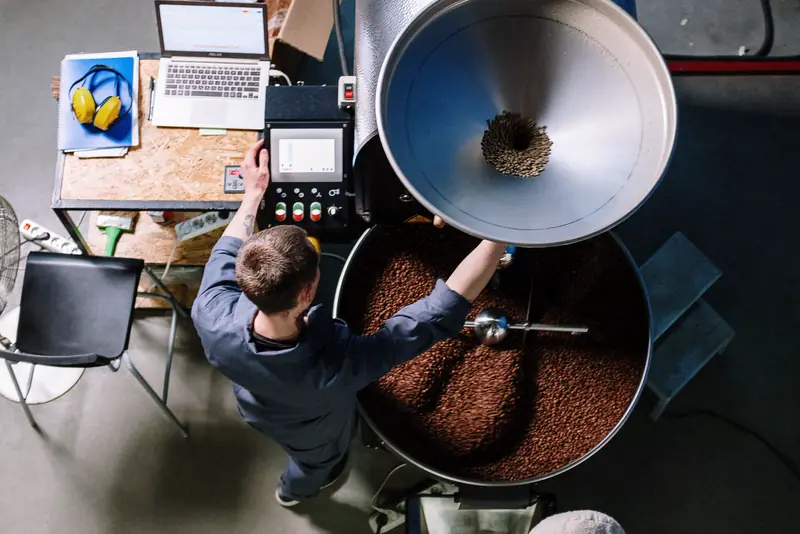A roaster checks a batch at the roasting machine, seen from above
