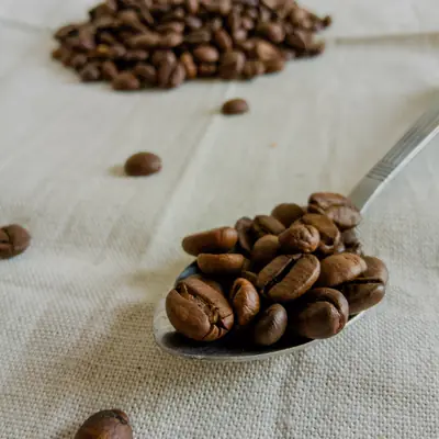A spoon of whole roasted coffee beans on linen