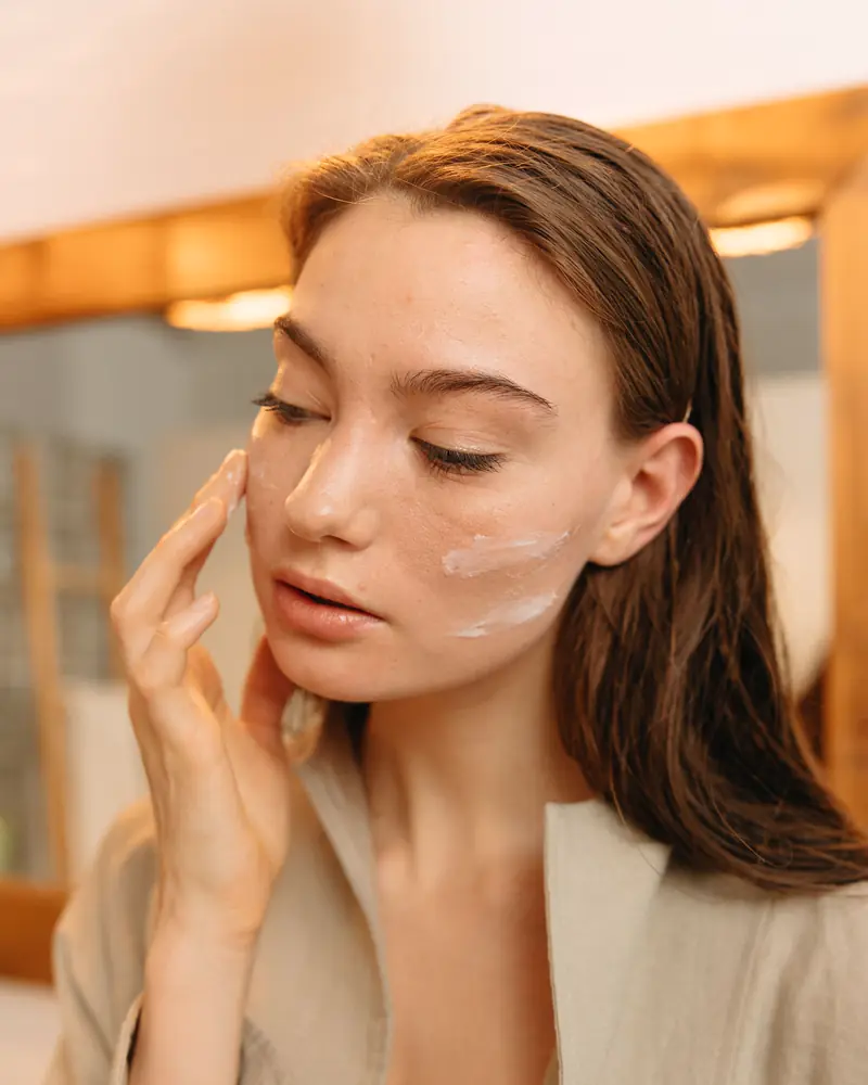 A woman smooths product onto her cheek in soft daylight