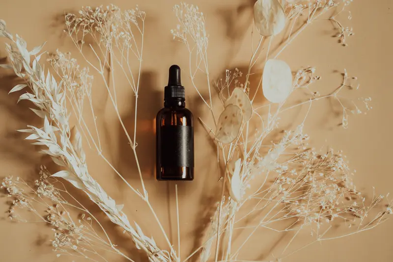 A glass dropper bottle laid among dried desert grasses and seed heads