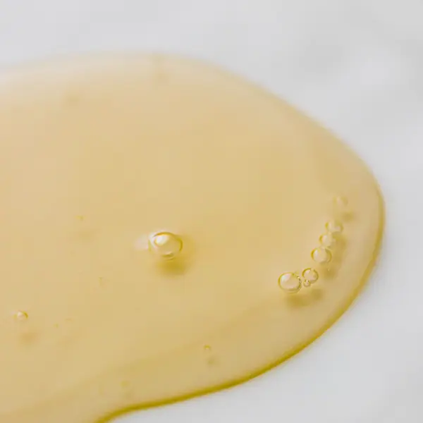 A single drop of golden serum on a white surface, showing the texture