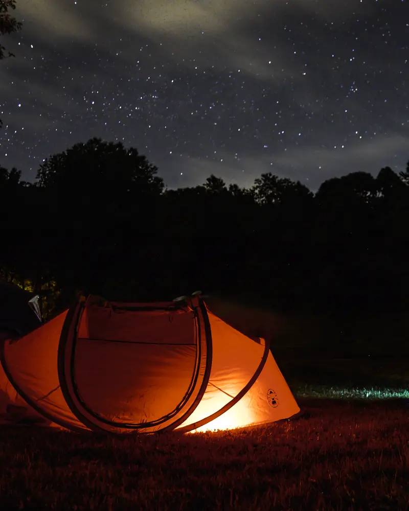 An orange tent glows under a starry night sky