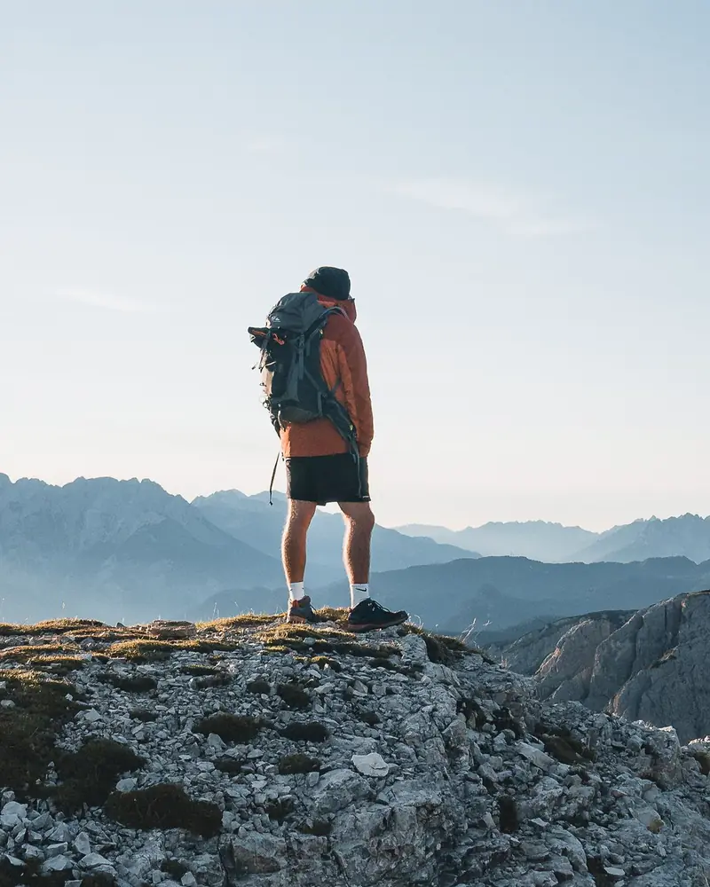 A hiker with a pack stands on a rocky ridge above a valley