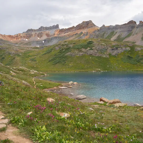 A hiker walks a trail beside an alpine lake in the San Juan Mountains