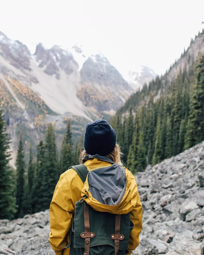 A backpacker in a yellow jacket carries the pack across a rocky alpine slope
