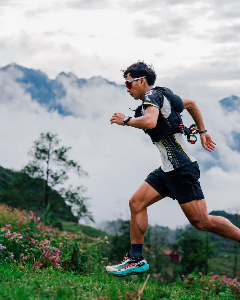 A trail runner in a vest strides along a misty mountain path