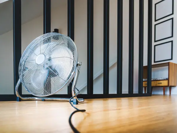 Floor fan running on a wood floor in a bright room