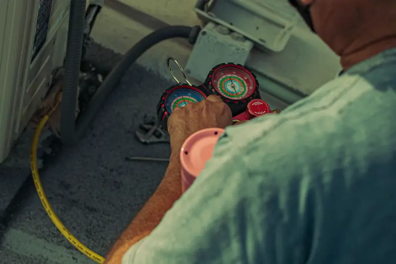 Technician reading refrigerant gauges beside an outdoor AC unit during a tune-up