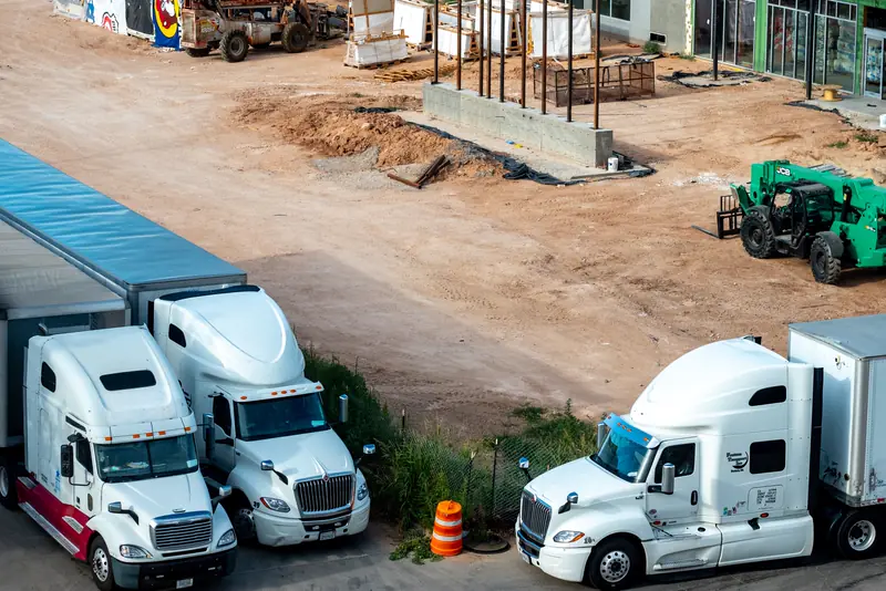 Three white semi trucks parked at a busy construction site