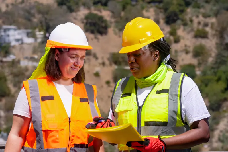 Two engineers in hard hats review plans on a construction site