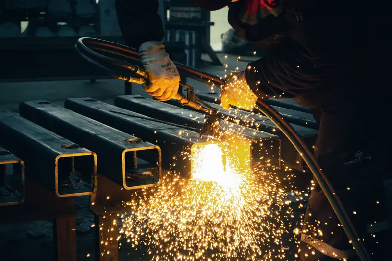A welder works on steel beams as sparks fly in a factory