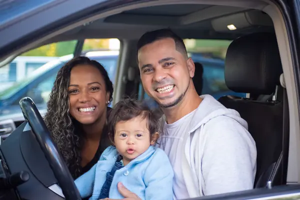 A smiling couple and their toddler sitting in the front seat of their car