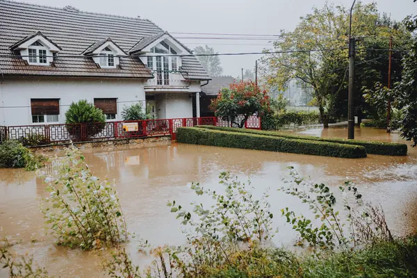 Floodwater covering the front yard of a suburban house after heavy rain
