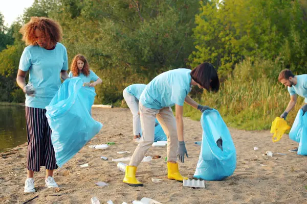 Volunteers in matching shirts collect trash along a sandy shoreline