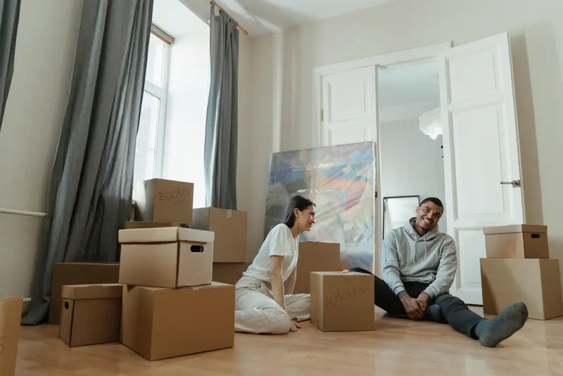 A couple sits on the floor of their new apartment among moving boxes