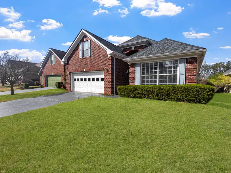 A red brick house with a thick, evenly mowed front lawn under a blue sky