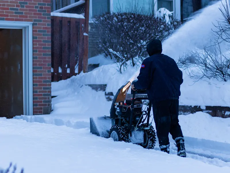 A worker clearing a snowy sidewalk with a snow blower