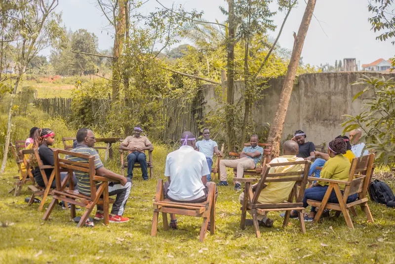 A group of adults seated in a circle of chairs in a shady garden