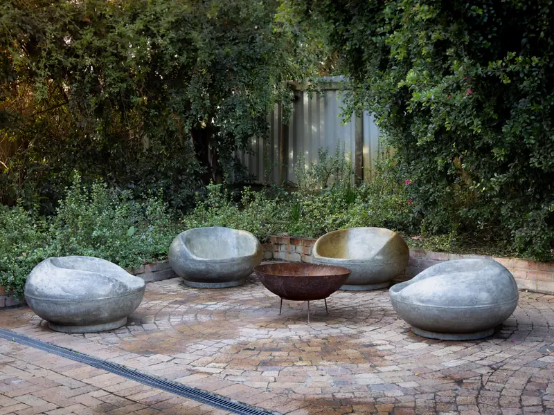 Sculpted stone seats around a steel fire bowl on a paved court surrounded by shade planting