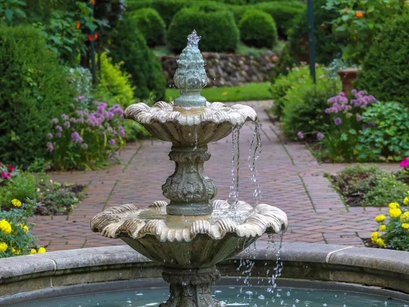 A tiered stone fountain at the center of a formal garden with brick paths