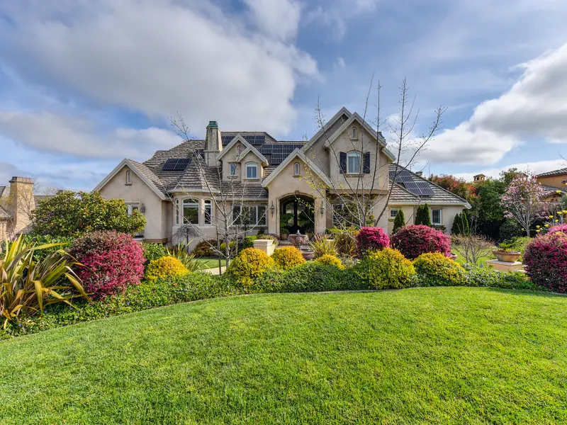 A stone house behind a deep front garden of flowering shrubs and a fresh lawn