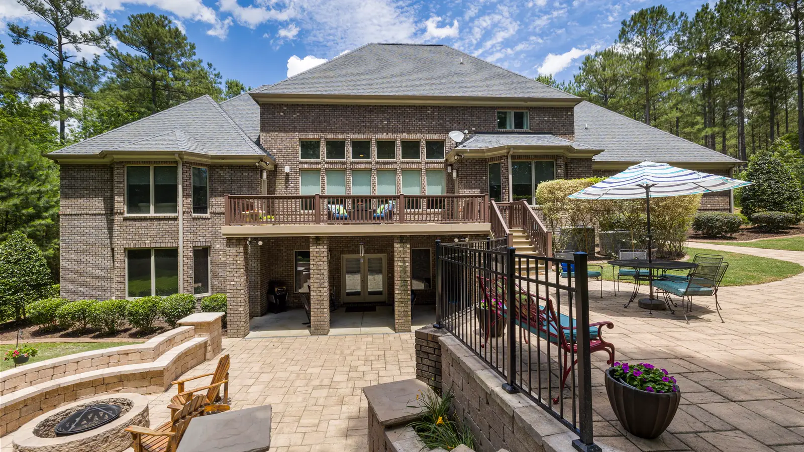 A brick house above a wide stone terrace with a fire pit, seat walls and a green lawn