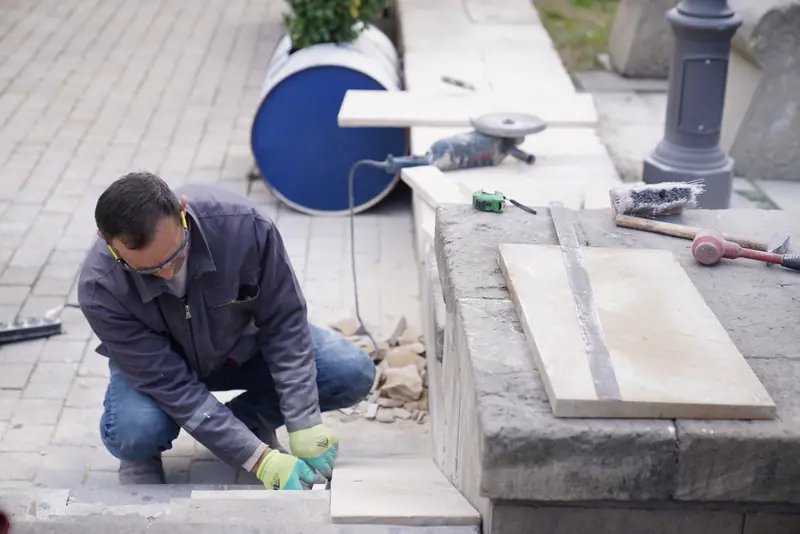 A mason in gloves setting stone tiles on a new terrace