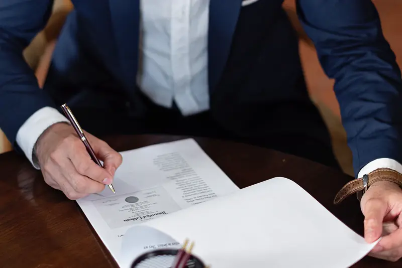 A man in a suit signs a document at a wooden desk