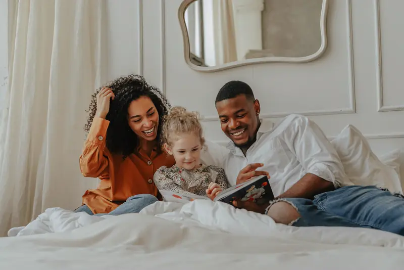 Two parents read a book with their toddler on a bed at home