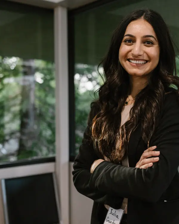 Priya Raman smiling with arms crossed by a window