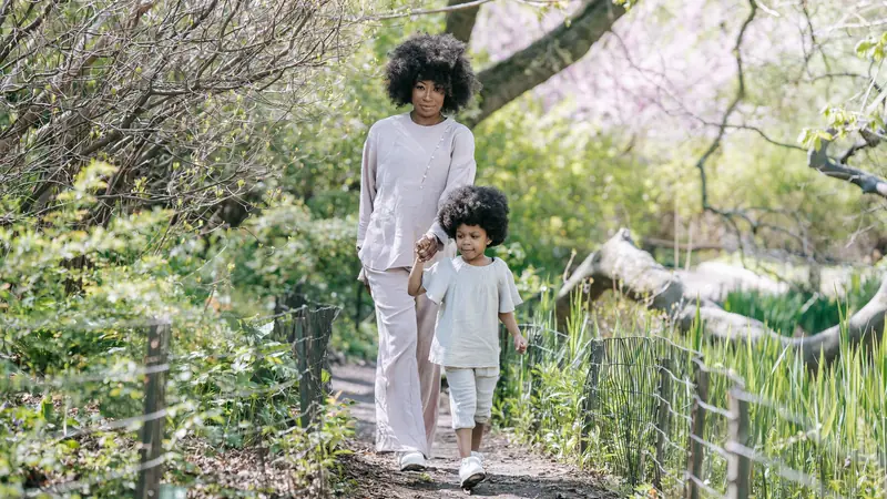 A mother and daughter walk along a green, sunlit garden path