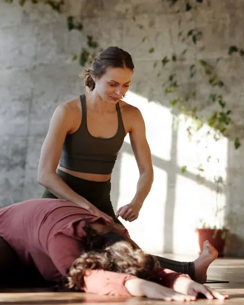 A therapist places her hands on a client's back as the client rests in a forward stretch.
