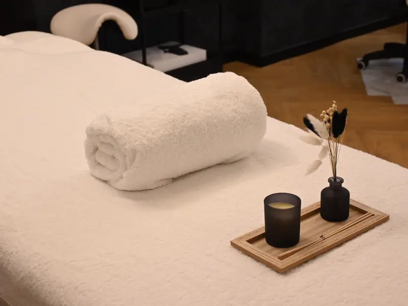 A treatment table with a rolled white towel, a candle and a small vase.