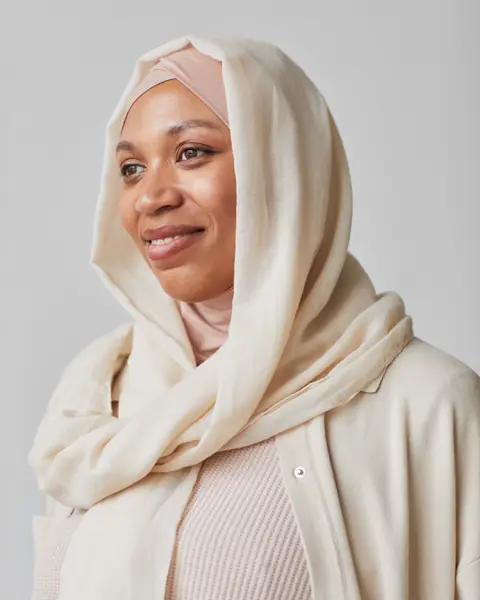 A woman in a cream headscarf and sweater smiles.
