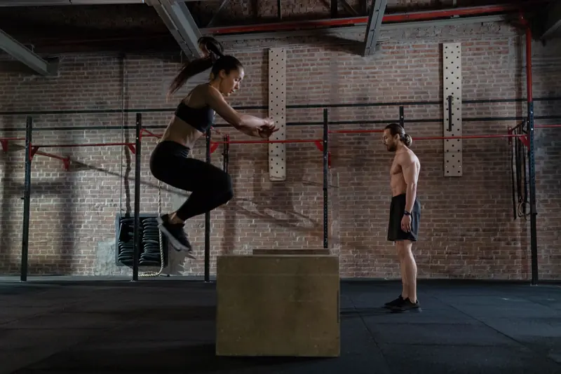 An athlete jumps onto a box while a coach watches.
