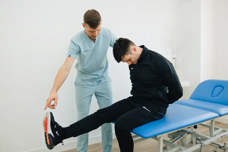 A therapist coaches a patient through a stretch on a treatment table.