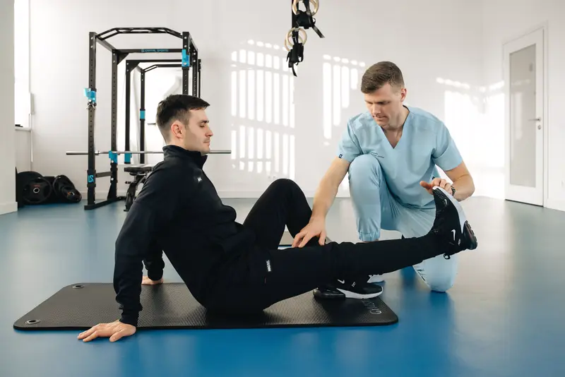 A therapist guides a patient through a leg exercise on the clinic floor.