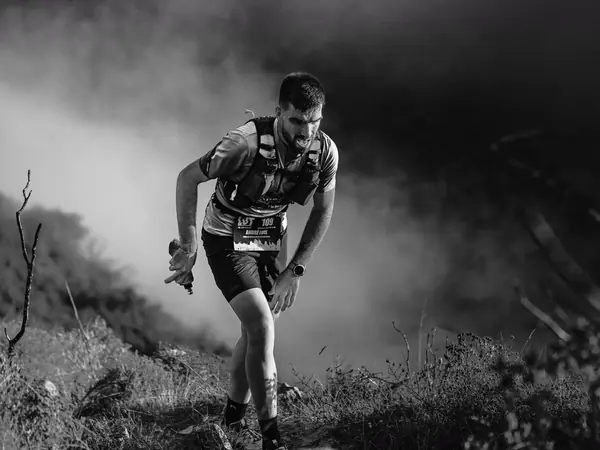 A trail runner climbs a rocky mountain path.
