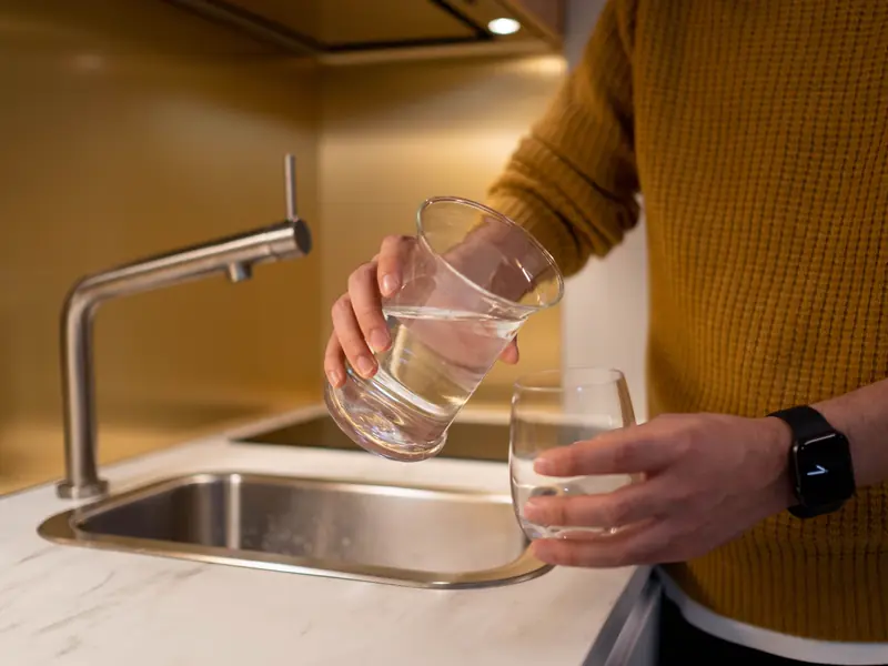 Someone filling a glass from a pitcher beside a kitchen sink