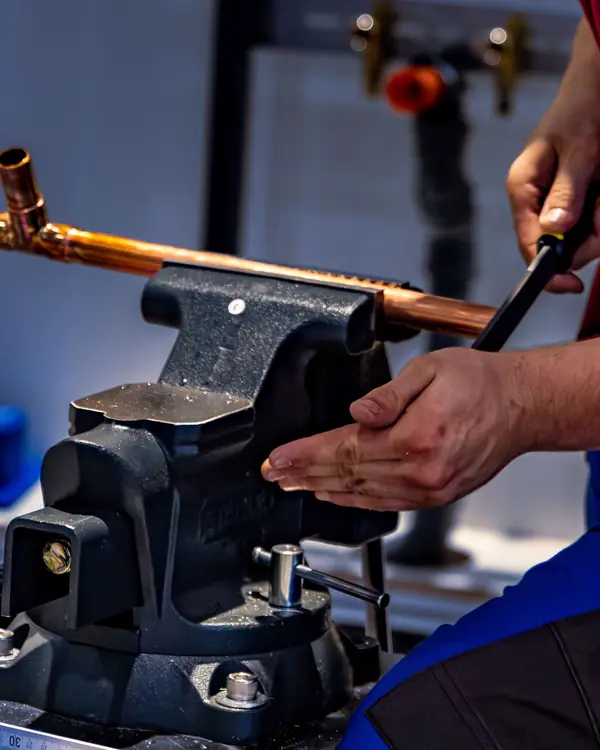 A Hartley plumber bending copper pipe in a bench vise