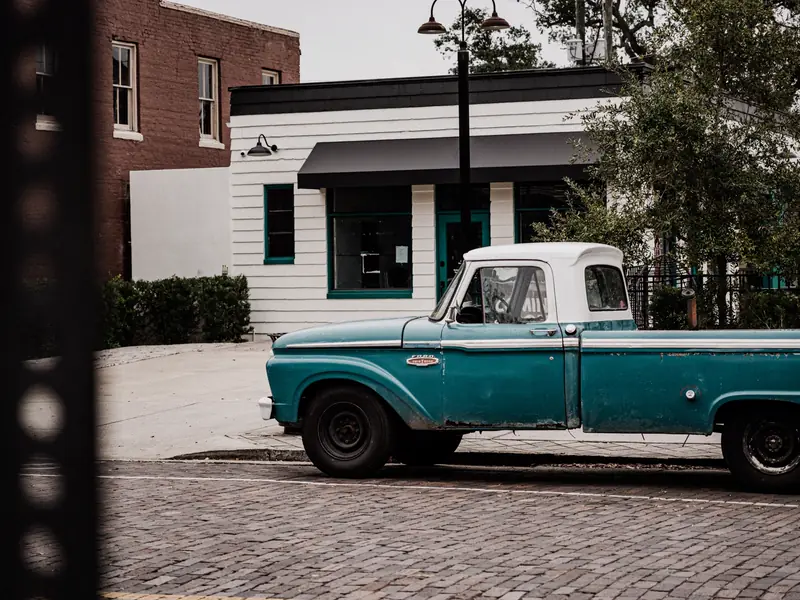 A teal 1960s pickup truck parked on a brick street